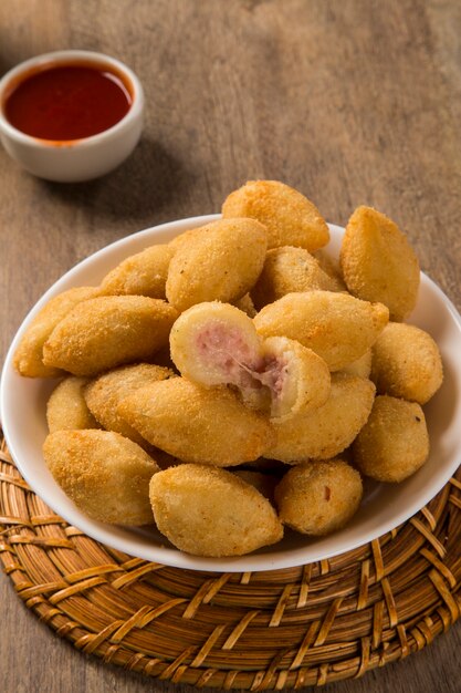 Foto petisco brasileiro frito com presunto de queijo em fundo de madeira.