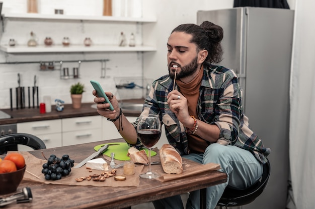 Petisco de vinho. Homem simpático e simpático comendo queijo delicioso enquanto bebe vinho em casa