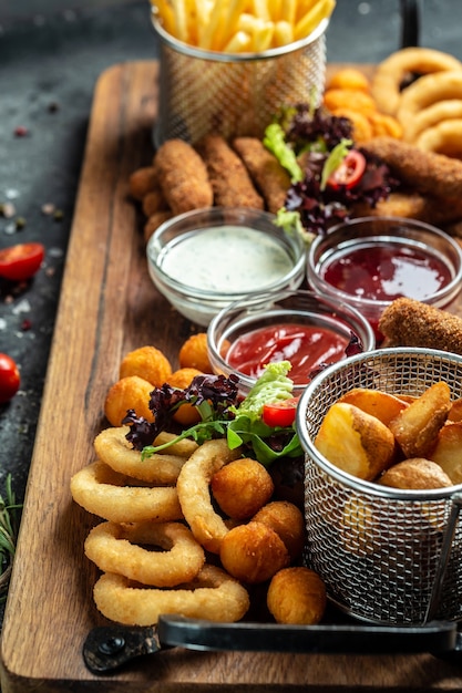 Petiscos de boteco em palitos de muçarela frita, rodelas de cebola, batata frita, nuggets de frango e molho. imagem vertical. vista do topo. lugar para texto