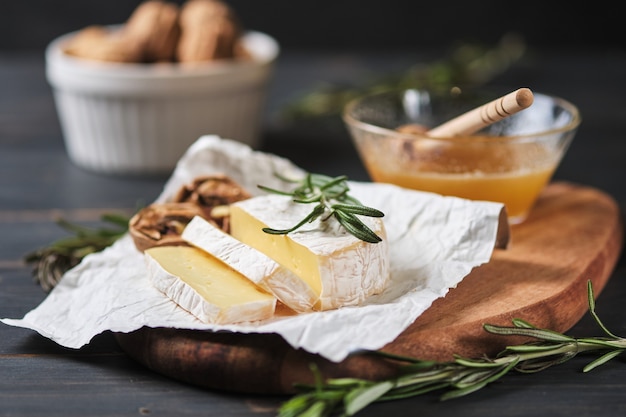 Petiscos deliciosos. Close-up de queijo brie em uma placa de madeira. Mel, queijo, nozes e ervas