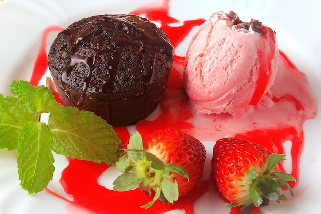 Petit gateau con helado en plato blanco con fresa sobre mesa de madera rústica