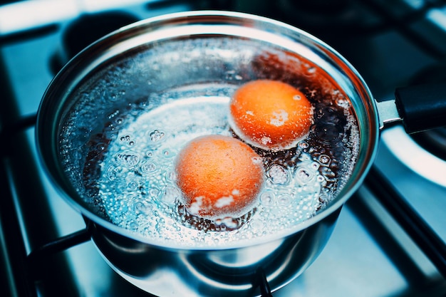 Pfanne aus Edelstahl mit kochenden Eiern Frühstück in Wasser auf einem Gastofen