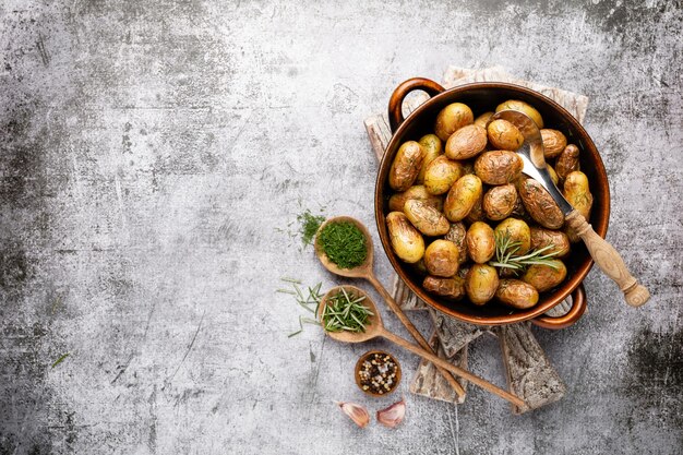 Pfanne gefüllt mit Bratkartoffeln auf rustikalem Holztisch Die Zutaten sind rohe Kartoffeln, Rosmarin, Dill, Salz, Pfeffer und Knoblauch