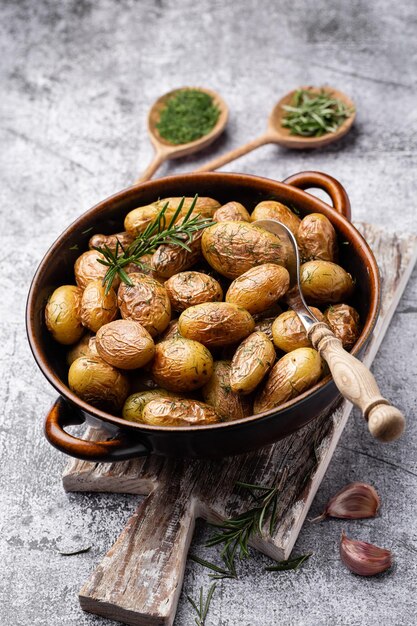 Pfanne gefüllt mit Bratkartoffeln auf rustikalem Holztisch Die Zutaten sind rohe Kartoffeln, Rosmarin, Dill, Salz, Pfeffer und Knoblauch