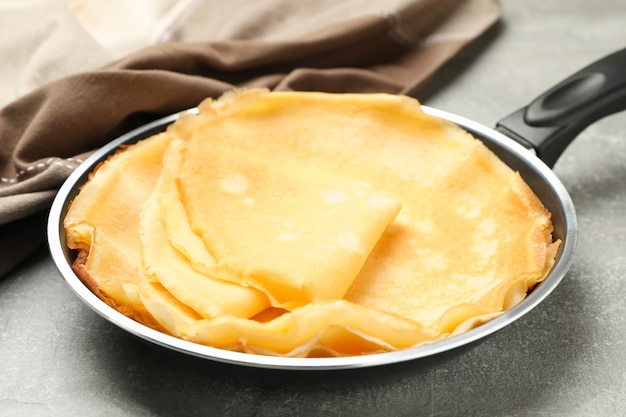 Pfanne mit dünnen Pfannkuchen und Küchentuch auf grauem Hintergrund