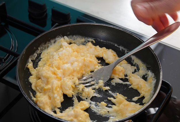 Pfanne mit einer Gabel Rührei auf dem Herd mischen