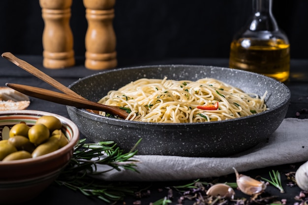 Pfanne mit gekochten italienischen Nudeln. Traditionelle Spaghettimahlzeit mit Gemüse und Oliven auf schwarzer rustikaler Oberfläche