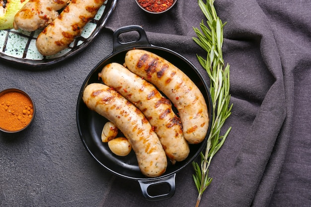 Pfanne mit leckeren Grillwürsten und Gewürzen auf Dunkel