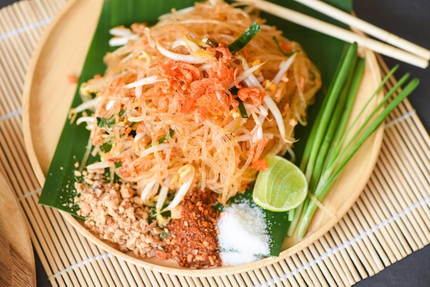 Pfannengerichte Nudel Pad Thai auf Teller serviert auf dem Esstisch Essen, thailändisches Essen gebratene Nudeln im thailändischen Stil mit Garnelen Sojasprossen und Garnierung Erdnüsse Chili Puderzucker Zitrone Limette - Ansicht von oben