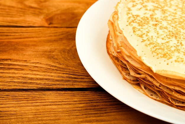 Pfannkuchen auf einem Teller auf einem Holztisch. Ein großer Stapel frischer Pfannkuchen. Köstliche gesunde frische Pfannkuchen. Platz für Werbung, Logo, Schriftzug, Layout, Mockup.