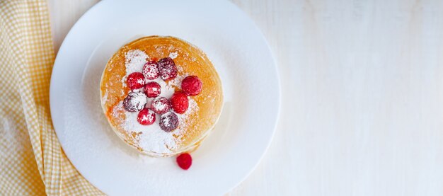 Pfannkuchen auf einem weißen Teller mit Früchten und Puderzucker auf einem hölzernen Hintergrund