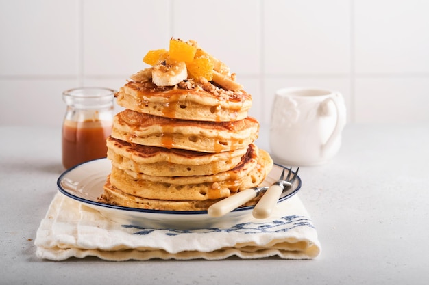 Pfannkuchen. Hausgemachter flauschiger Pfannkuchen mit Banane, Walnuss und Karamell zum Frühstück auf hellem Betonhintergrund. Leckere Pfannkuchen für ein traditionelles amerikanisches Frühstück. Selektiver Fokus. Attrappe, Lehrmodell, Simulation.