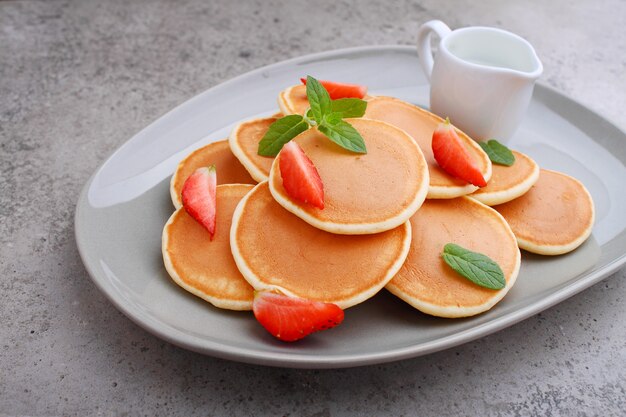 Pfannkuchen in einem Teller mit Erdbeeren, die mit Minze auf einem Betontisch verziert sind