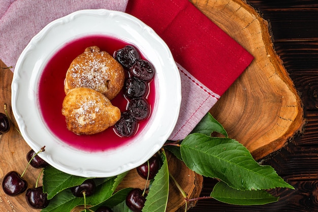 Pfannkuchen in Kirschsauce in einem Teller und Kirschbeeren mit grünen Blättern auf einem Holzbrett