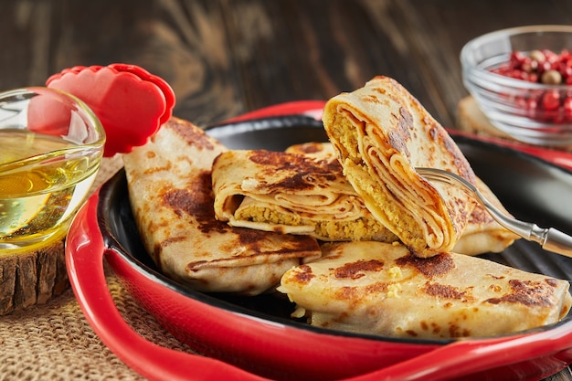 Pfannkuchen mit Fleisch auf Gabel mit Butter und Zange auf Teller auf dunklem Holzhintergrund