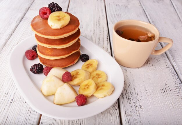 Pfannkuchen mit Früchten und Beeren auf Teller mit Tasse Tee auf Holztisch