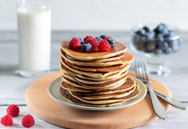 Pfannkuchen mit Himbeeren Heidelbeeren Milch auf Holzbrett mit Messer und Gabel