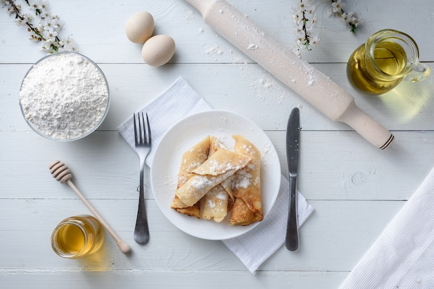 Pfannkuchen mit Hüttenkäse auf einem weißen hölzernen Hintergrund. Schuss mit Honig, Sonnenblumenkernen, Mehl und Eiern. Ein traditionelles Frühstück.