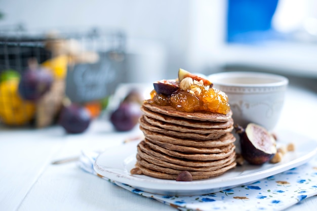 Pfannkuchen mit Marmelade und Feigen auf einem weißen Teller und einer Tasse Kaffee auf einem weißen Hintergrund