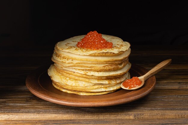 Pfannkuchen mit rotem Kaviar Ein Haufen Pfannkuchen Pfannkuchen auf einem Teller und mit Kaviar auf einem Holzlöffel Roter Kaviar