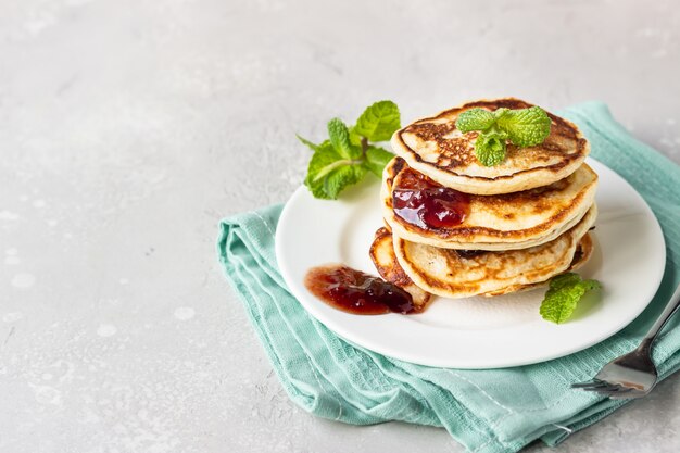 Pfannkuchen mit roter Beerenmarmelade und Minze, hellgrauer Steinhintergrund amerikanische Küche. Frühstück.