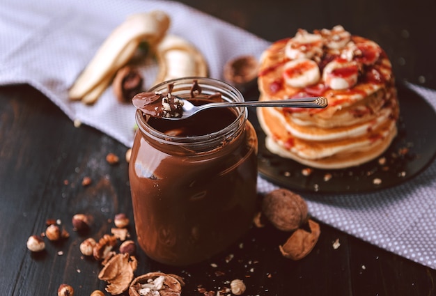 Pfannkuchen mit Schokolade und Nusspaste, Walnüssen und Banane auf einem schwarzen Teller