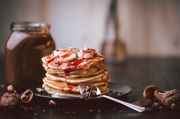 Foto pfannkuchen mit schokolade und nusspaste, walnüssen und banane auf einem schwarzen teller