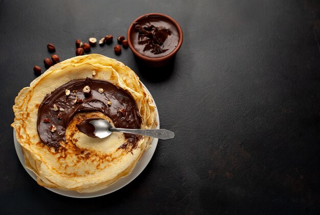 Pfannkuchen mit Schokoladenpaste und Haselnüssen, auf einem weißen Teller auf einem Hintergrund aus Beton, Schiefer mit Kopierraum für Ihren Text