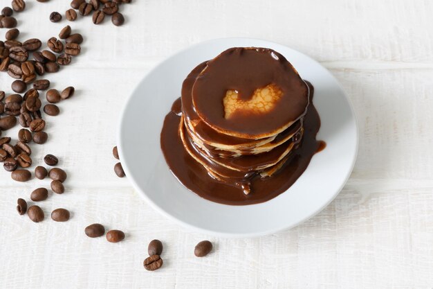 Pfannkuchen mit Schokoladensirup und Kaffeebohnen auf weißem Tisch