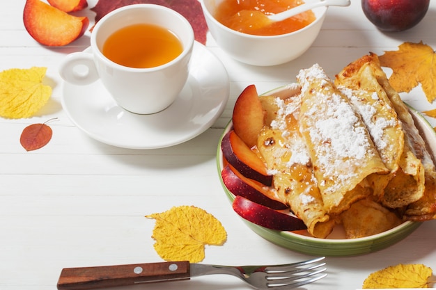 Pfannkuchen mit Tee und Pflaumen auf weißem Holztisch