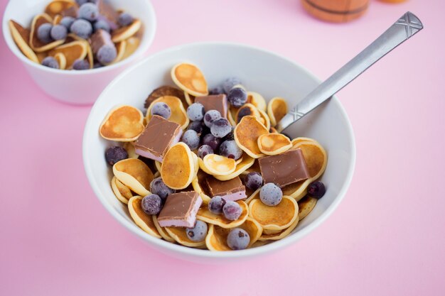 Pfannkuchen-Müsli in einem Teller mit Blaubeeren und Schokolade auf einem rosa Tisch Trendiges modernes Frühstück mit kleinen Pfannkuchen