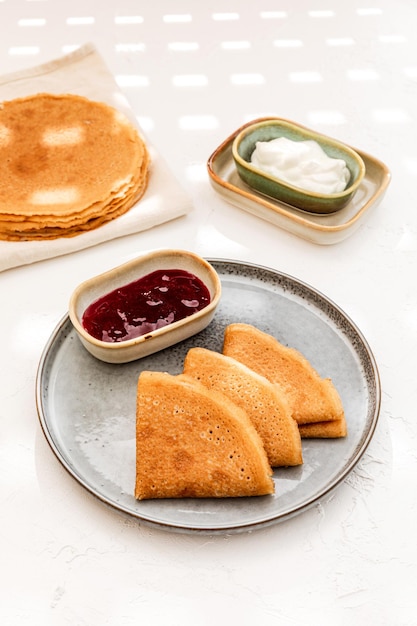 Pfannkuchen serviert auf einem Teller mit Sauerrahm und Beerenmarmelade ein Stapel Pfannkuchen im Hintergrund weißer Hintergrund mit hartem Licht