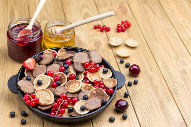 Pfannkuchen und Beeren in der Pfanne. Honig und Marmelade auf dem Tisch. Helle Holzoberfläche. Draufsicht. Speicherplatz kopieren