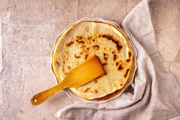 Pfannkuchen und ein Holzspatel liegen auf einem runden Keramikteller und einer Leinenserviette auf beigem Vintage-Hintergrund