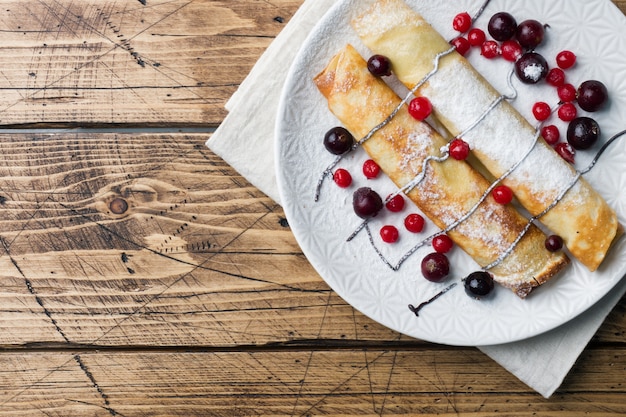 Pfannkuchenrohr mit Schokolade und Beeren auf einer Platte. Hölzerner Hintergrund Platz kopieren