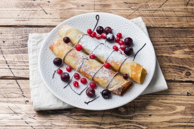 Pfannkuchenrohr mit Schokolade und Beeren auf einer Platte. Hölzerner Hintergrund