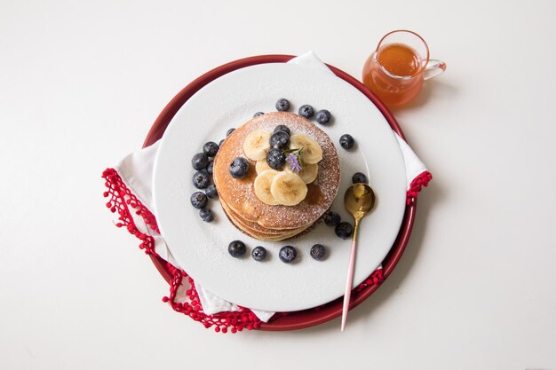 Pfannkuchenstapel mit Bananen- und Blaubeerbelag und Bienenhonig-Frühstücksessen