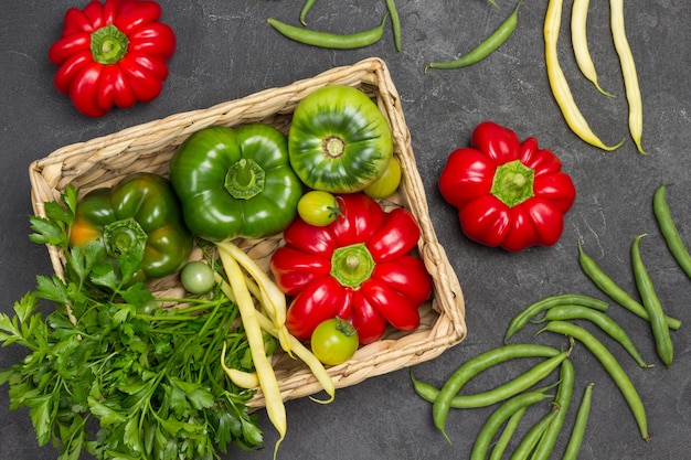 Pfeffer, grüne Tomate und Petersilie im Weidenkorb. Rote Paprika und grüne Bohnen auf dem Tisch. Flach liegen. Schwarzer Hintergrund