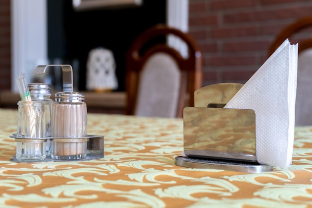 Pfefferstreuer und Salzstreuer Auf dem Tisch in einem Café steht ein Serviettenständer Der Tisch im Restaurant ist mit einer Tischdecke bedeckt Weiße Papierservietten auf einem Ständer und einem Glasbehälter mit Zucker