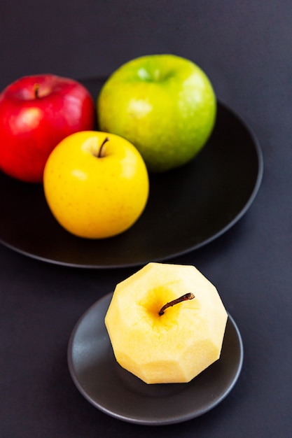 Äpfel grün gelb rot und Apfel ohne Schale an einer schwarzen Wand