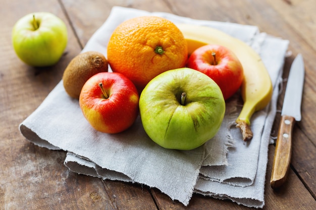 Äpfel, Orange, Banane und Kiwi auf rustikalem Holztisch.