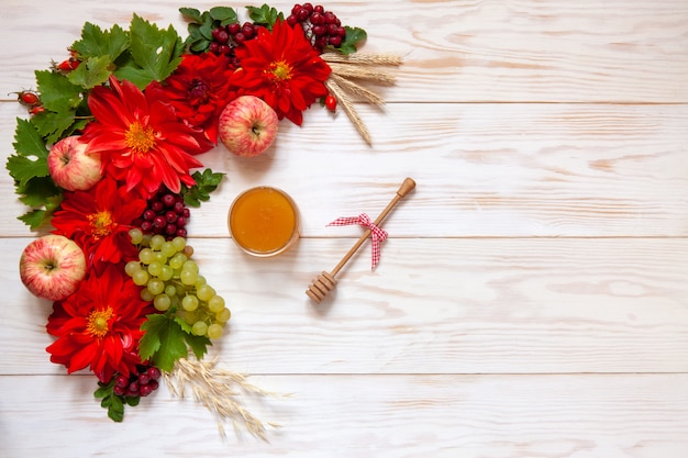 Äpfel, Trauben, rote Dahlienblumen, rote Vogelbeeren und Honig mit Kopienraum