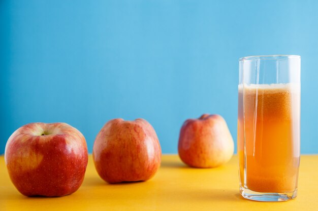 Äpfel und ein Glas natürlicher Apfelsaft auf gelbblau