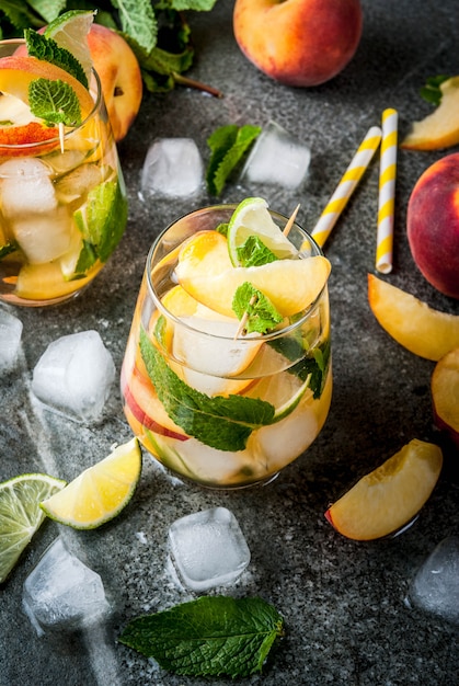 Pfirsich Mojito mit Limette, Pfirsich und Minze auf einem dunklen Steintisch.