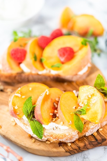 Pfirsich-Ricotta-Toasts, garniert mit Walnüssen, frischer Minze und Himbeeren auf einem Holzschneidebrett.