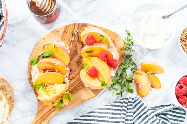 Pfirsich-Ricotta-Toasts, garniert mit Walnüssen, frischer Minze und Himbeeren auf einem Holzschneidebrett.