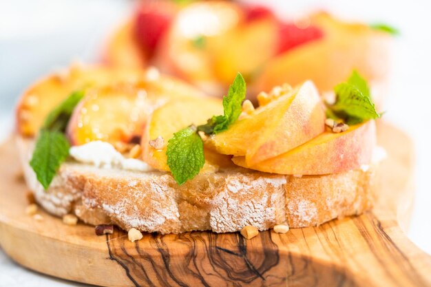 Pfirsich-Ricotta-Toasts, garniert mit Walnüssen, frischer Minze und Himbeeren auf einem Holzschneidebrett.