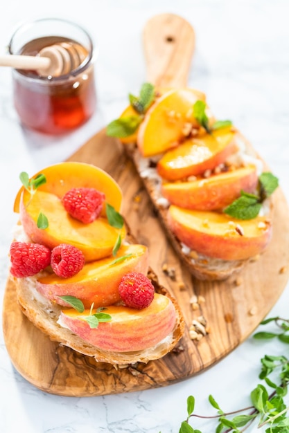 Pfirsich-Ricotta-Toasts, garniert mit Walnüssen, frischer Minze und Himbeeren auf einem Holzschneidebrett.