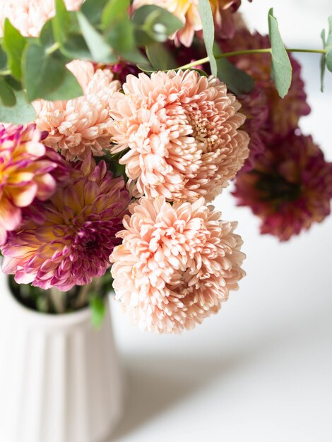 Pfirsichastern und Burgunder mit gelben Dahlien mit Eukalyptuszweigen in einer Vase.