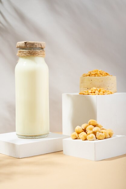 Pflanzliche Erbsenmilch in einer Flasche und Kichererbsen in handgemachter Keramikschale auf weißem Podest, Sockel auf beigem Hintergrund. Schatten. Glutenfreies, laktosefreies veganes Produkt. Moderne Komposition. Platz kopieren